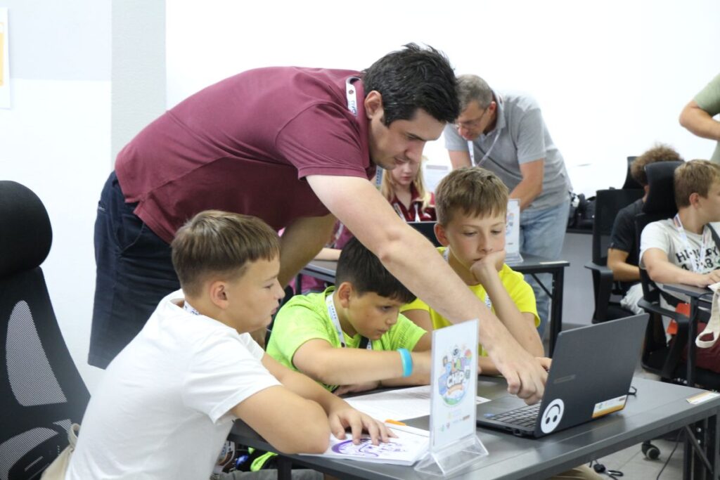 Young participants work through a laptop-based challenge with guidance from an instructor during the PLAY CHIP summer camp in Ukraine. (Photo credit: TaiwanICDF)